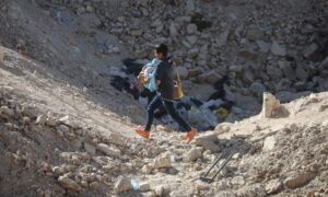 A boy carrying a baby walked from Lebanon to Syria on foot at the al-Masnaa border crossing after prior Israeli strikes closed the road to vehicles - October 14, 2024 (Reuters)