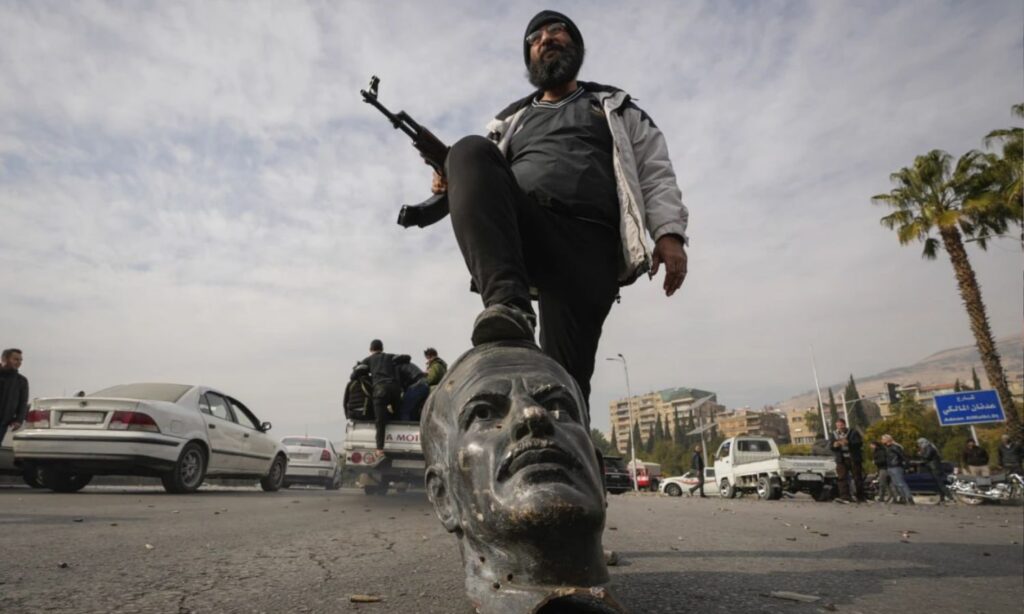 A fighter from the Syrian opposition factions stands on a statue of Hafez al-Assad in Damascus - December 8, 2024 (AFP)