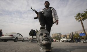 A fighter from the Syrian opposition steps on a statue of Hafez al-Assad in Damascus - December 8, 2024 (AFP)