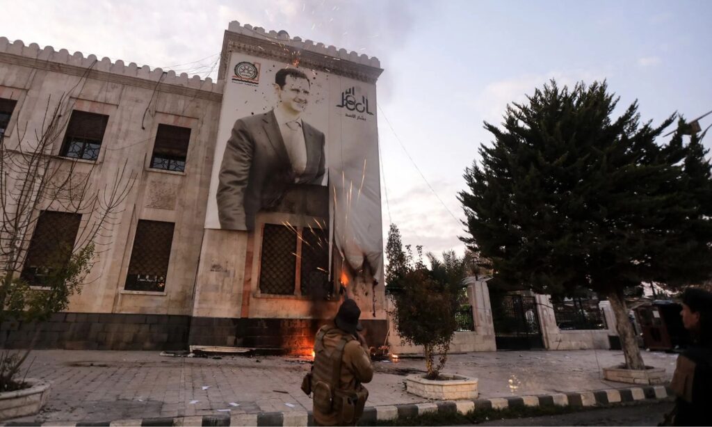 A fighter from the Syrian opposition factions shoots at a picture of Bashar al-Assad in the Hama municipality building - December 5, 2024 (Bakr al-Qasim/Getty Images/Bloomberg)