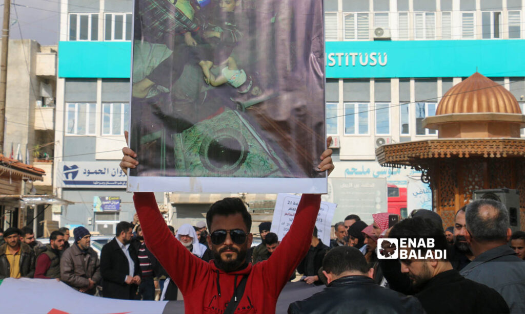 A protester in the city of Azaz holds a sign reminding of the chemical massacre in Douma - February 3, 2023 (Enab Baladi/Dayan Junpaz)