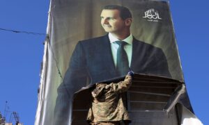 An element of the Military Operations Administration tears a picture of Bashar al-Assad in Aleppo - November 30, 2024 (CNN)