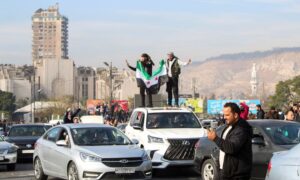 Men holding the Syrian revolution flag atop a car in Damascus celebrating the fall of the Assad regime - December 8, 2024 (Reuters)