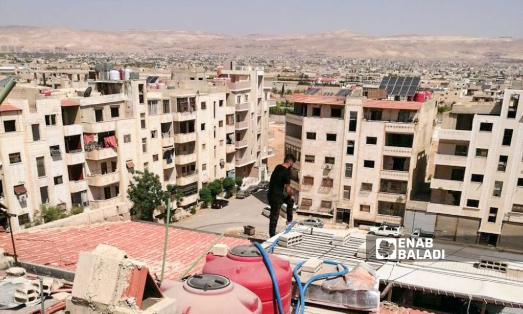 A man fills a water tank on the roof of a building in Ashrafiyat Sahnaya, rural Damascus – May 7, 2025 (Enab Baladi/Noor Hamza)