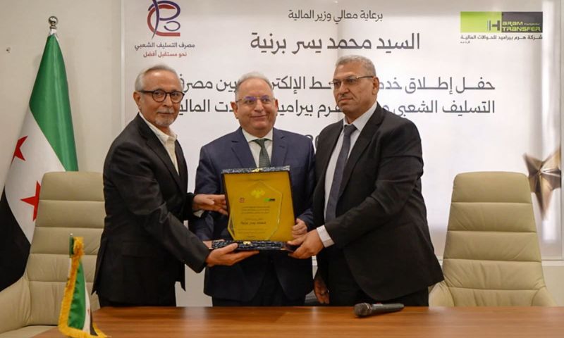 Popular Credit Bank Director General Adnan Hassan and Al-Haram Board Chairman Fuad Asi present a commemorative shield to Syrian Finance Minister Mohammed Yisr Barnieh during the launch ceremony for the electronic link between the bank and the company, August 19, 2026. (Syrian finance minister/Facebook)